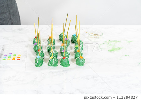 Decorating cactus cake pops with luster dust, sugar glower, and white sprinkles for the Cinco de Mayo celebration. Decorating cactus cake pops with luster dust, sugar glower, and white sprinkles for the Cinco de Mayo celebration. 112294827
