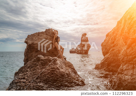 Woman swimsuit sea. Attractive blonde woman in a black swimsuit enjoying the sea air on the seashore around the rocks. Travel and vacation concept. 112296323