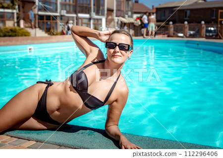Bikini-clad woman enjoys poolside relaxation. Poolside ambiance. Capturing woman's relaxed time near pool. Bikini-clad woman enjoys poolside relaxation. Poolside ambiance. Capturing woman's relaxed time near pool. 112296406