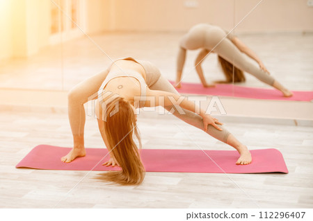Girl does yoga. Young woman practices asanas on a beige one-ton background. 112296407