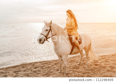 A white horse and a woman in a dress stand on a beach, with the A white horse and a woman in a dress stand on a beach, with the 112296409
