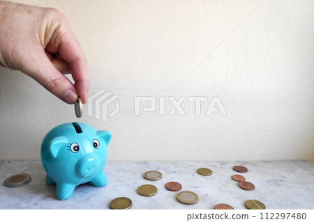 Feeding the piggy bank with euro coins Feeding the piggy bank with euro coins 112297480