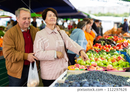 Elderly man and a woman buy berries at an open air market Elderly man and a woman buy berries at an open air market 112297626