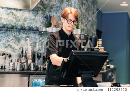 Young waiter serving customer at cash point in cafe. Man working with POS terminal. Student working part-time. Problems of unemployment and Job opportunities for youth. Small business vacancies. 112298330