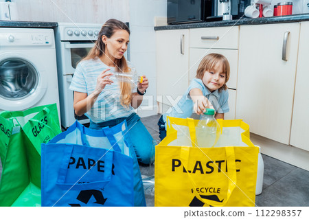 Mother is teaching kid how to recycle help the boy aware environmental importance - mom educates son sort garbage into different bins on kitchen. Family sorting garbage at home. Concept of recycling. 112298357