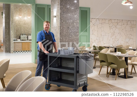 Portrait of a worker in the cafeteria with a cart for dirty dishes Portrait of a worker in the cafeteria with a cart for dirty dishes 112298526