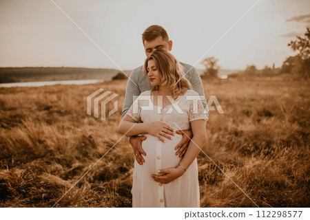 husband hugs pregnant wife keep his hands on big round tummy. 112298577