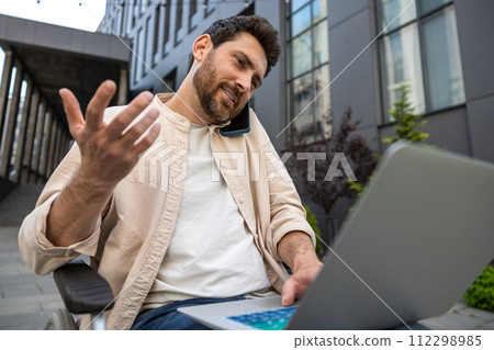 Man on a wheelchair working on laptop and talking on the phone 112298985