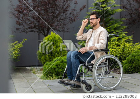 Young bearded man in a wheelchair working on laptop Young bearded man in a wheelchair working on laptop 112299008
