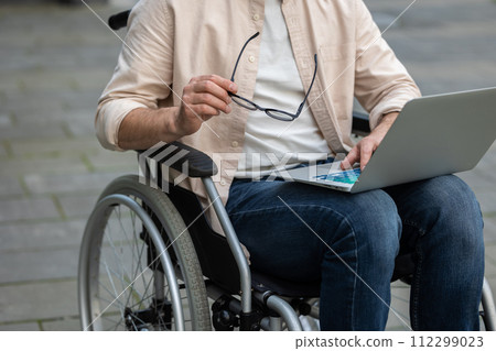 Disabled self-employed man working on laptop while sitting in wheelchair in hospital yard Disabled self-employed man working on laptop while sitting in wheelchair in hospital yard 112299023