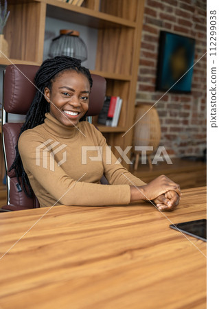 Happy satisfied multicultural woman sitting at table in office interior Happy satisfied multicultural woman sitting at table in office interior 112299038