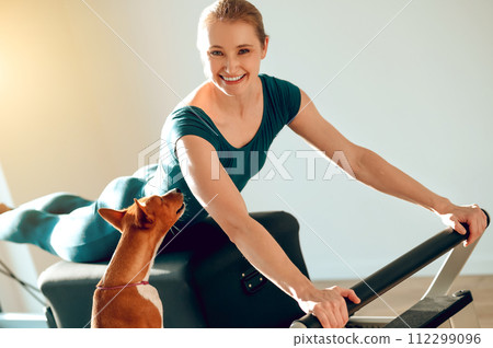 Smiling woman doing sports exercises in Pilates studio with her dog 112299096