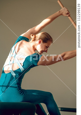 Attractive woman doing stretching workout with wooden exercise stick at Pilates studio Attractive woman doing stretching workout with wooden exercise stick at Pilates studio 112299139