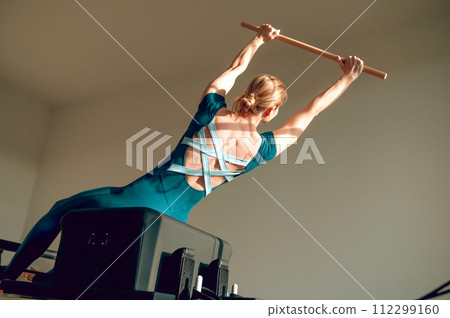 Fit woman exercising with bar in gym training her arms and back in Pilates studio 112299160