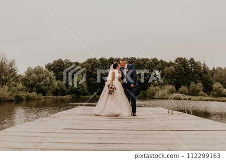 Newlyweds kissing hugging on wooden pier bridge on lake 112299163
