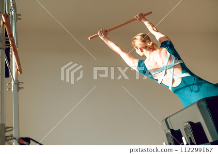 Attractive woman doing stretching workout with wooden exercise stick at Pilates studio Attractive woman doing stretching workout with wooden exercise stick at Pilates studio 112299167