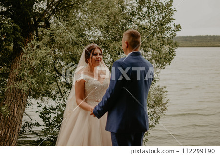 Newlyweds hold hands and look at each other near river Newlyweds hold hands and look at each other near river 112299190