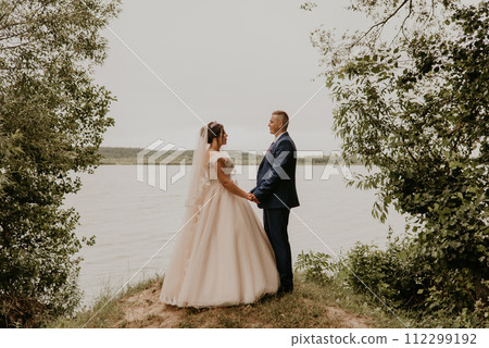 Newlyweds hold hands and look at each other near river Newlyweds hold hands and look at each other near river 112299192