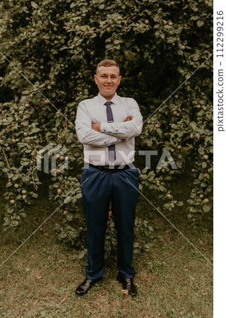 successful businessman groom in classic clothes stands his hands clasped together in nature successful businessman groom in classic clothes stands his hands clasped together in nature 112299216