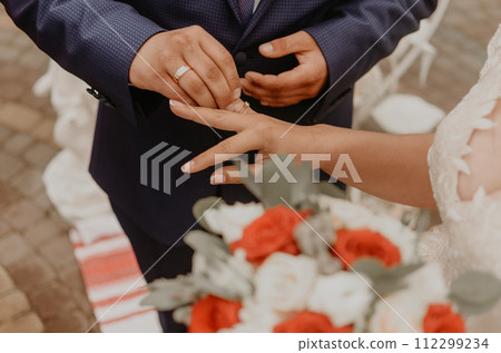 man puts a ring on woman ring finger as a sign of his love at a wedding man puts a ring on woman ring finger as a sign of his love at a wedding 112299234