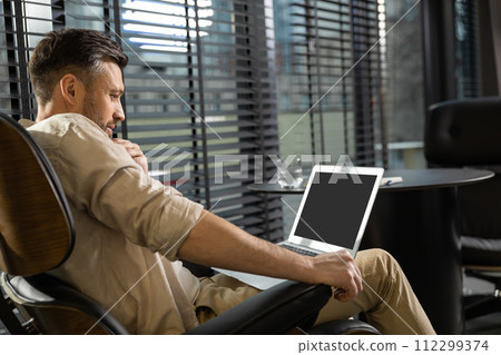 Young bearded man in casual clothes working on laptop Young bearded man in casual clothes working on laptop 112299374