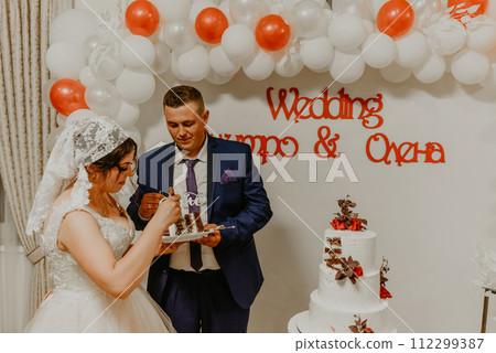 groom and bride at wedding cut their large multi-tiered white cake taste it fed from each other. 112299387