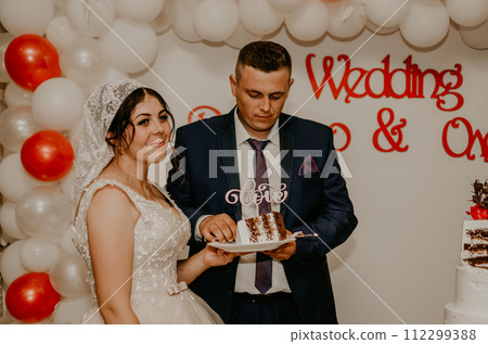 groom and bride at wedding cut their large multi-tiered white cake taste it fed from each other. groom and bride at wedding cut their large multi-tiered white cake taste it fed from each other. 112299388