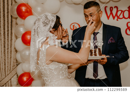 groom and bride at wedding cut their large multi-tiered white cake taste it fed from each other. 112299389
