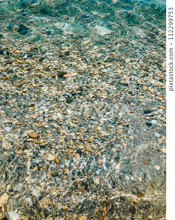 Close up sea waves stones shells beach summer day. top view above transparent water. Close up sea waves stones shells beach summer day. top view above transparent water. 112299753