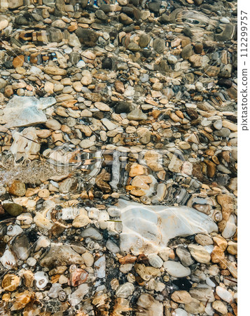 Close up sea waves stones shells beach summer day. top view above transparent water. Close up sea waves stones shells beach summer day. top view above transparent water. 112299757