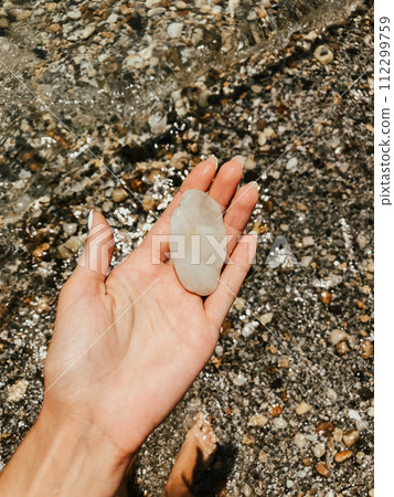 Woman hand manicure holding white beautiful stones above sea sandy summer beach. 112299759