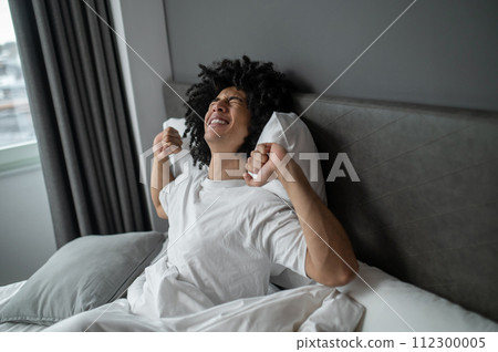 Curly-haired brunette young man waking up in a hotel bedroom Curly-haired brunette young man waking up in a hotel bedroom 112300005