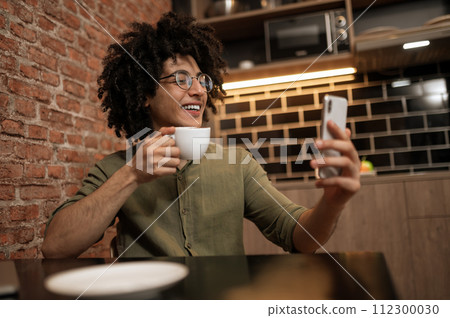 Young curly-haired man with a phone in hands having a video call Young curly-haired man with a phone in hands having a video call 112300030