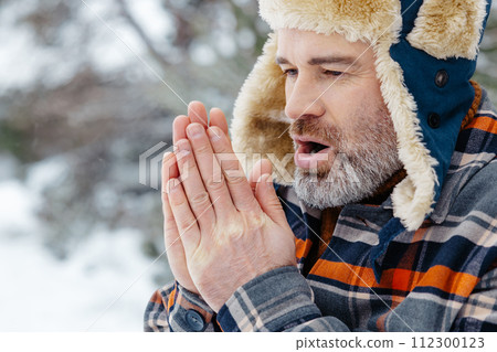 Mature man in warm hat warming his hands with his breath 112300123