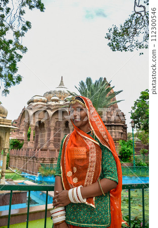 Indian Woman with beautiful face and orange sari posing with ruins in background Indian Woman with beautiful face and orange sari posing with ruins in background 112300546