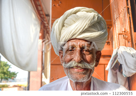 Elderly man with mustache and traditional Rajasthani turban smiling to camera 112300555