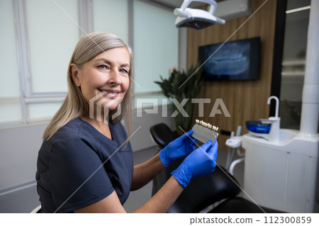 Caucasian woman doctor holding dental teeth shade guide chart in dentistry 112300859