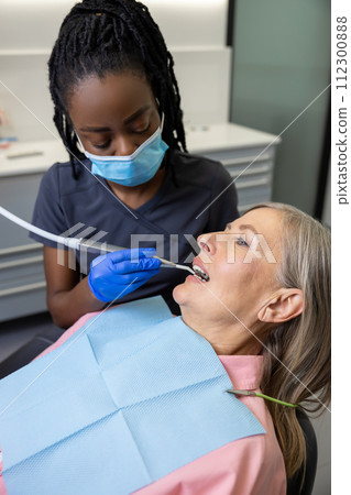 Doctor holding instrument tool for oral examination of middle aged female patient 112300888