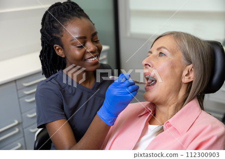 Woman patient sitting in dental chair at medical center while professional doctor fixing her teeth Woman patient sitting in dental chair at medical center while professional doctor fixing her teeth 112300903