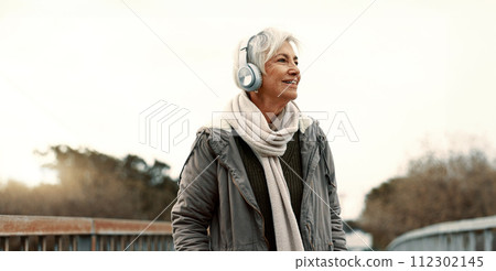 Senior woman, headphones and music outdoor, walking and wellness with audio streaming and energy. Podcast, listen to radio and sound with female person on city bridge, exercise and travel with tech Senior woman, headphones and music outdoor, walking and wellness with audio streaming and energy. Podcast, listen to radio and sound with female person on city bridge, exercise and travel with tech 112302145