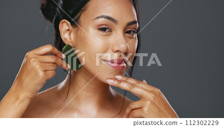 Woman, guasha and skincare for massage, facial and portrait or smile in studio by gray background. Happy model, cosmetics and dermatology in technique for beauty, self love and natural glow by tool 112302229