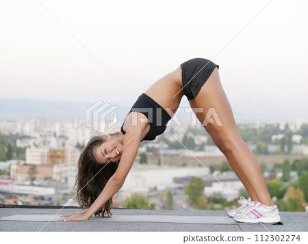 Woman, smile and warm up on rooftop for yoga, downward facing dog pose and urban city of Cape Town. Person, wellness and stretching body for balance to improve flexibility, mobility and peace of mind Woman, smile and warm up on rooftop for yoga, downward facing dog pose and urban city of Cape Town. Person, wellness and stretching body for balance to improve flexibility, mobility and peace of mind 112302274