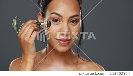 Woman, smile and facial roller for skincare or massage in studio by gray background. Happy model, cosmetics and dermatology for wellness, glow and tool for treatment on skin, beauty and health 112302594
