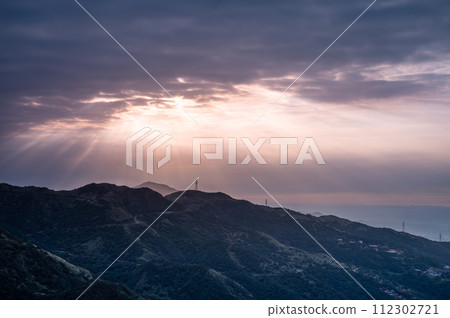 The sun shines through the clouds onto the mountain tops and the sea. 112302721