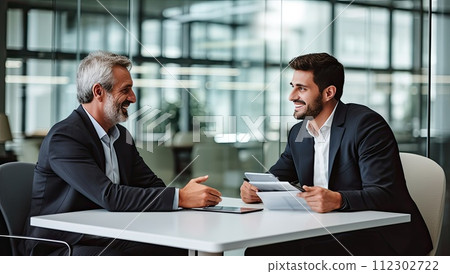 Two business people talking and smiling while sitting at the table in office 112302722