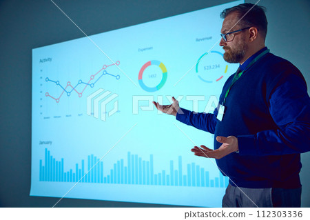 Entrepreneur gesturing while presenting his new ideas on meeting in conference hall standing near screen with charts. 112303336