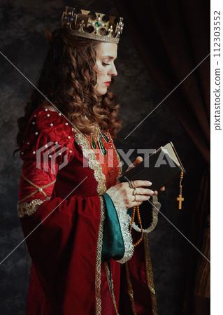 medieval queen in red dress with book, rosary and crown 112303552