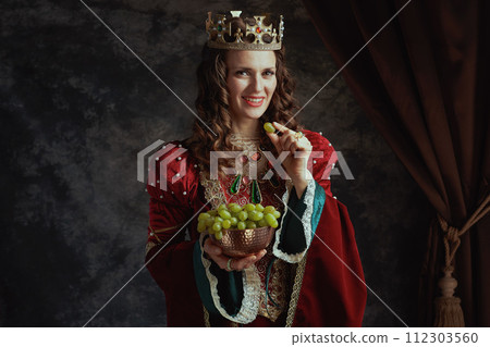 happy medieval queen in red dress with plate of grapes 112303560