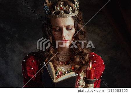 medieval queen in red dress with book, candle and crown medieval queen in red dress with book, candle and crown 112303565