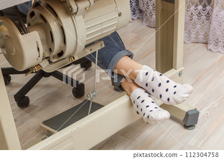 Female feet on the pedal of a sewing machine, motor 112304758